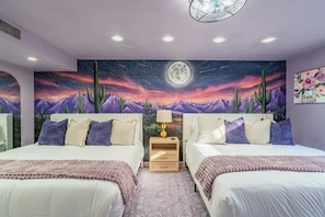 Een slaapkamer met twee bedden, een nachtkastje, een lamp en een muurschildering van een sterrenhemel met cactussen en een maan.