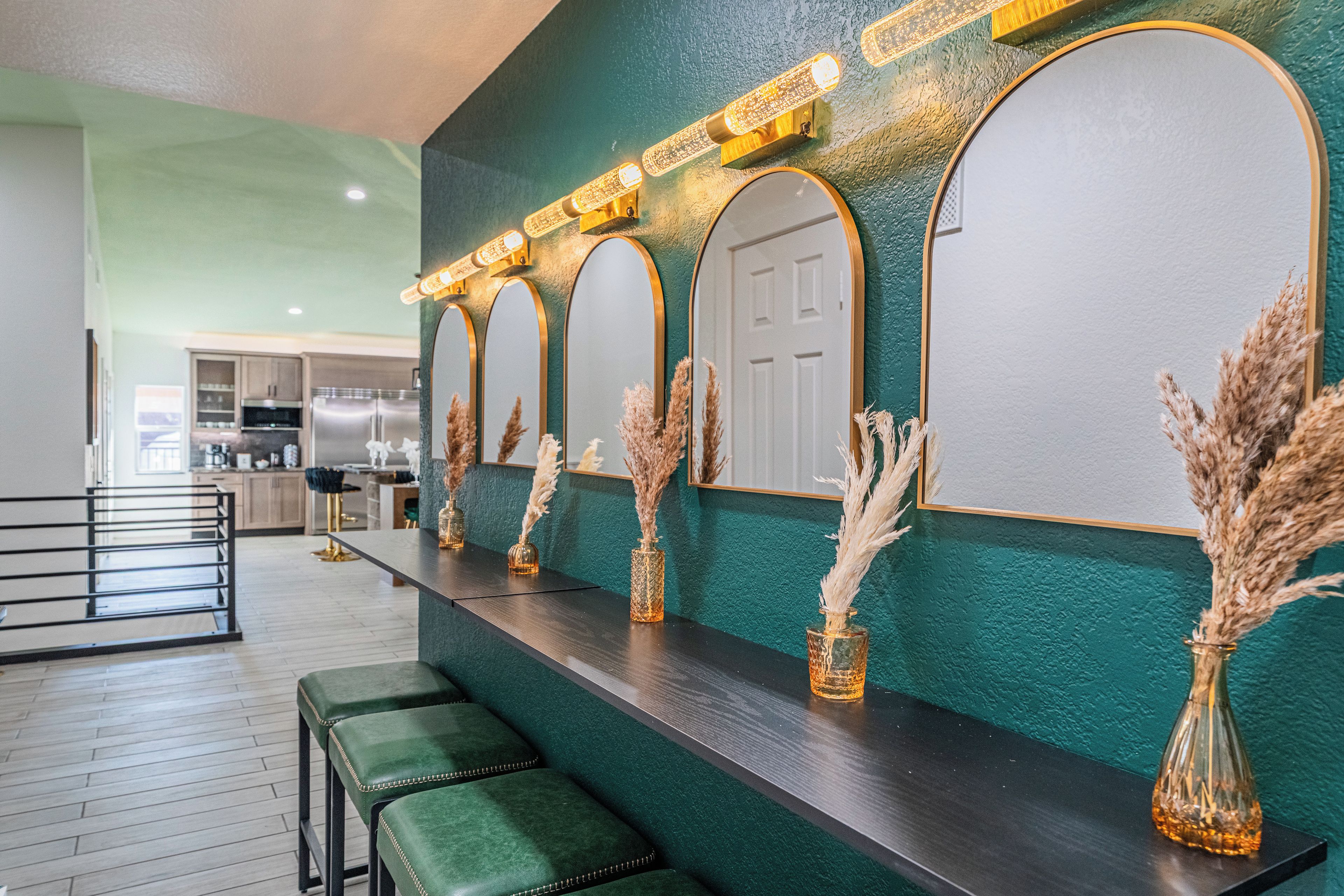 A bar area with a dark countertop, green upholstered bar stools, and decorative vases with pampas grass.