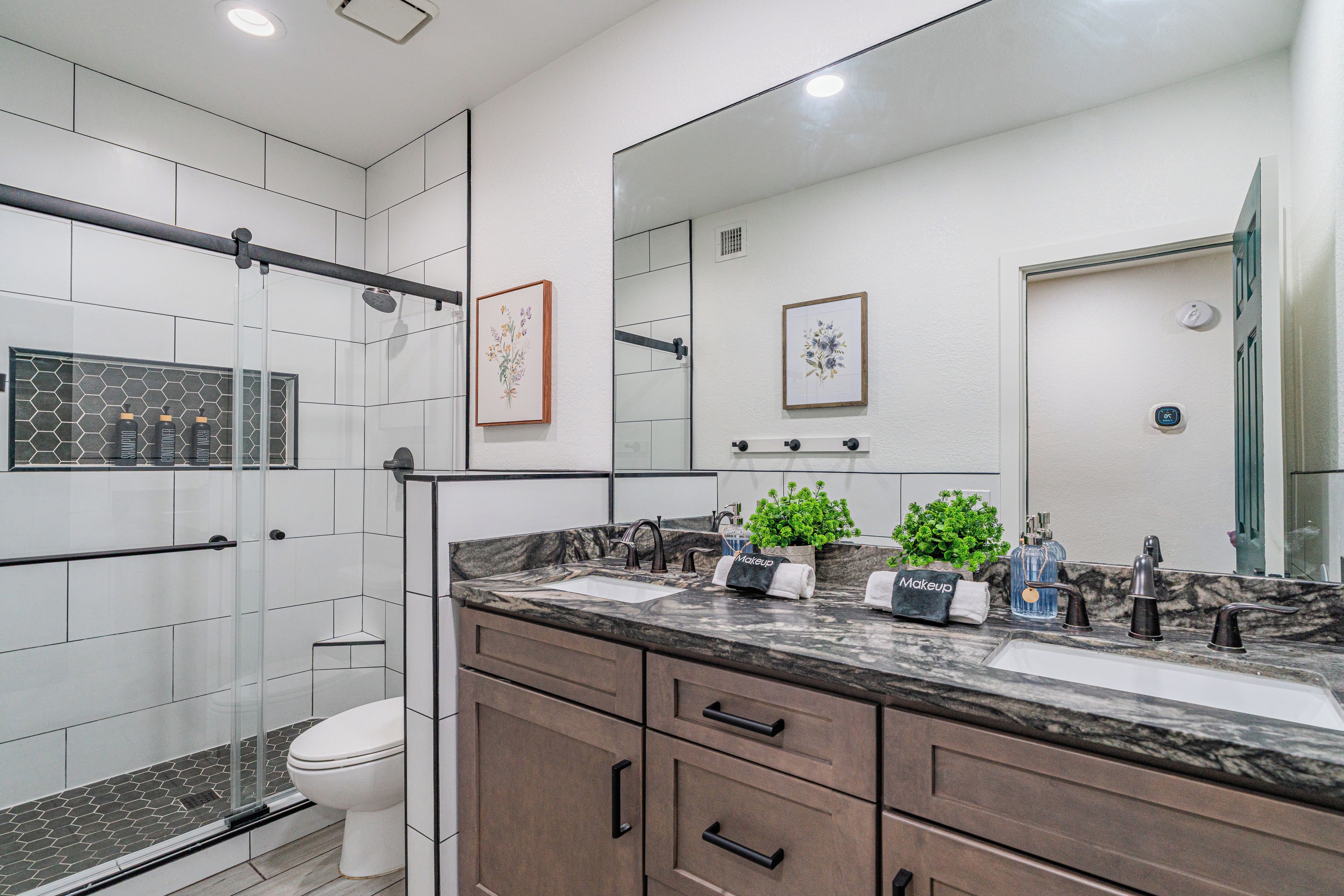 Ein modernes Badezimmer mit Duschkabine aus Glas, Toilette, Waschtisch mit Marmorplatte und zwei gerahmten Blumenbildern an der Wand.