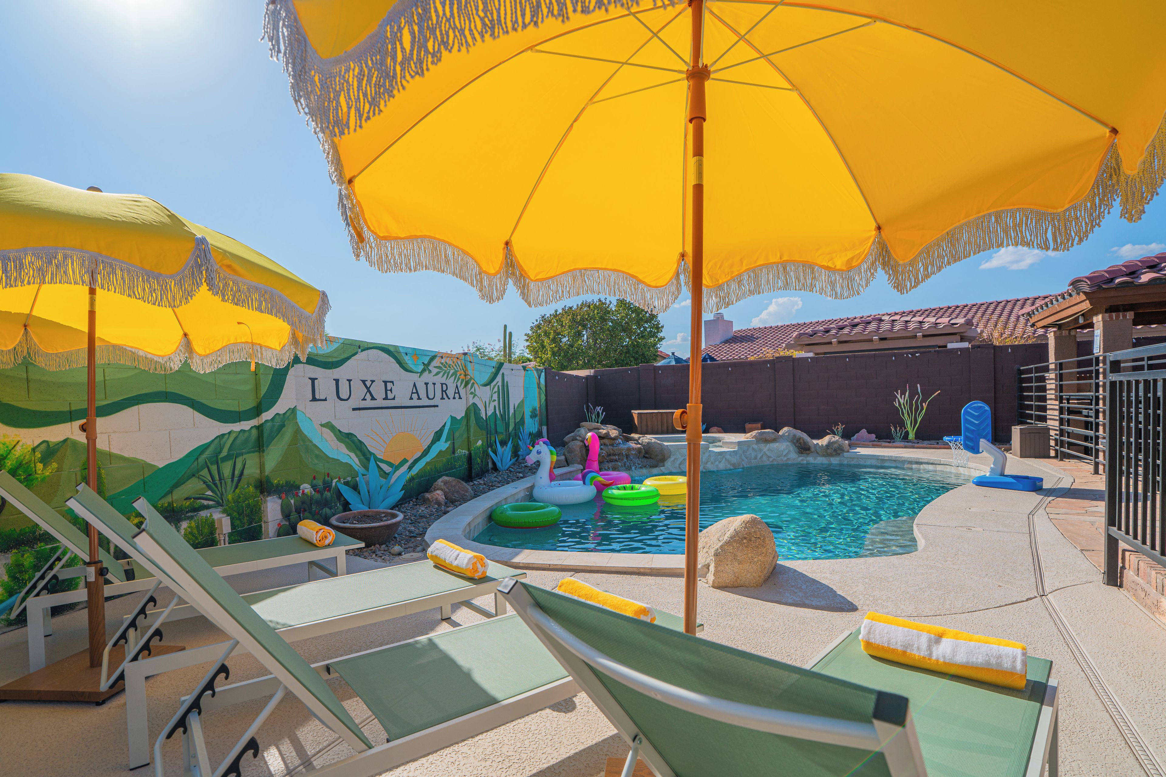A pool area with lounge chairs, umbrellas, and a mural with the text 'LUXE AURA'.