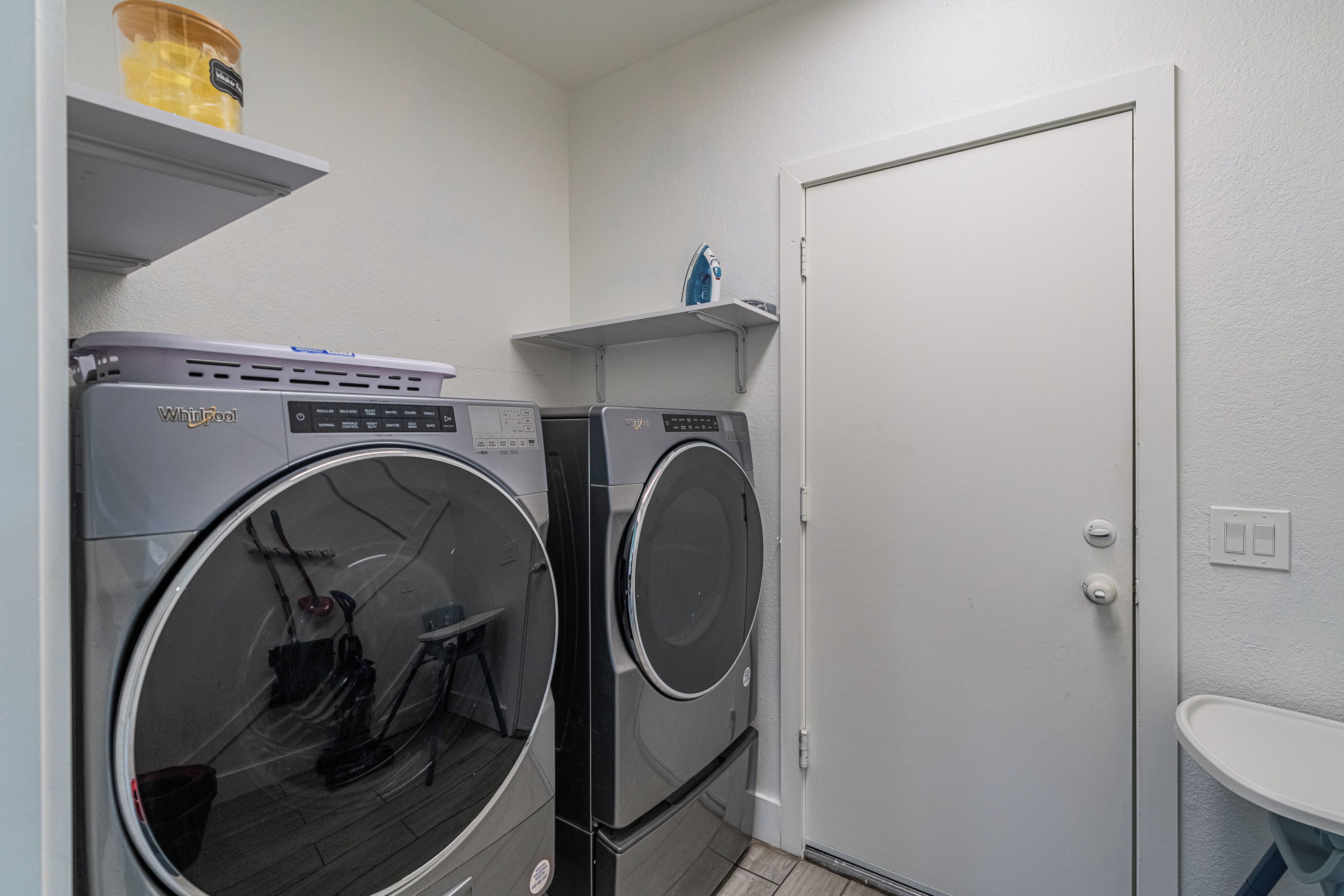 A laundry room with two front-loading Whirlpool washers, a shelf with a yellow container, and a white door.