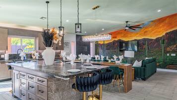 A modern kitchen with a large island, bar stools, and a dining area with green upholstered furniture.