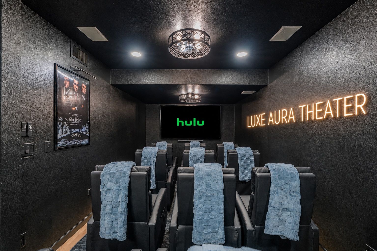 A theater with black walls, a large screen displaying 'hulu', and a sign that reads 'LUXE AURA THEATER'.
