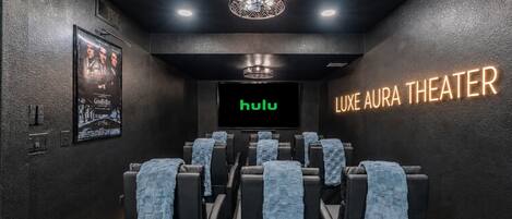 A theater with black walls, a large screen displaying 'hulu', and a sign that reads 'LUXE AURA THEATER'.