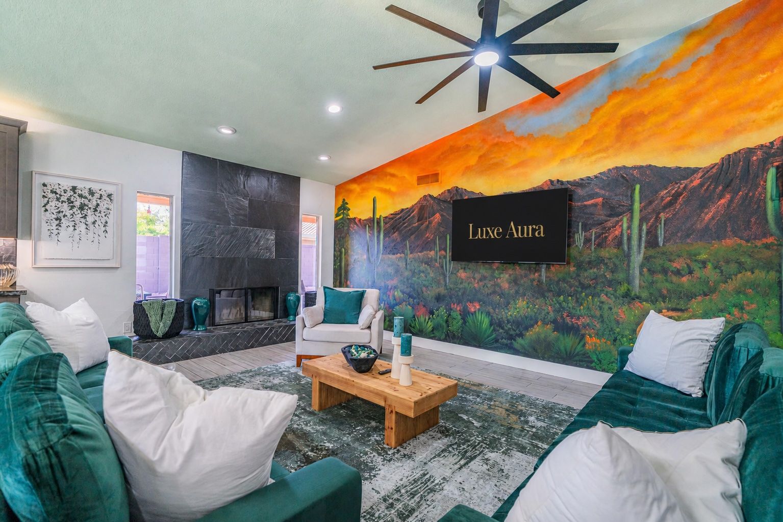 A living room with a fireplace, green sofas, a coffee table, and a mural with the text 'Luxe Aura'.