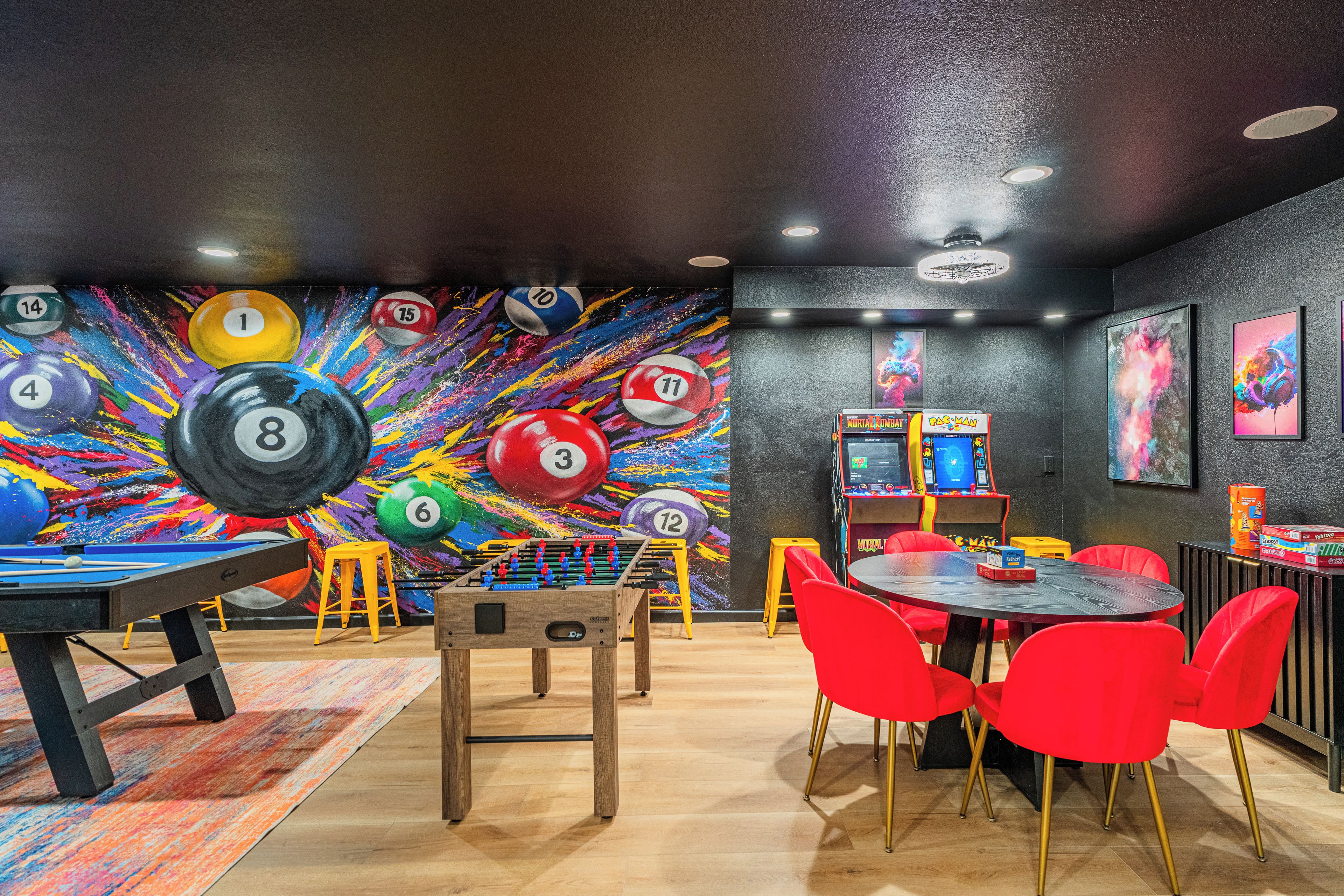Een kamer met een pooltafel, tafelvoetbal en een kleurrijke muurschildering met genummerde biljartballen.