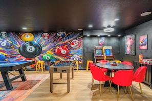 Una habitación con mesa de billar, mesa de fútbolín y un mural colorido con bolas de billar numeradas.