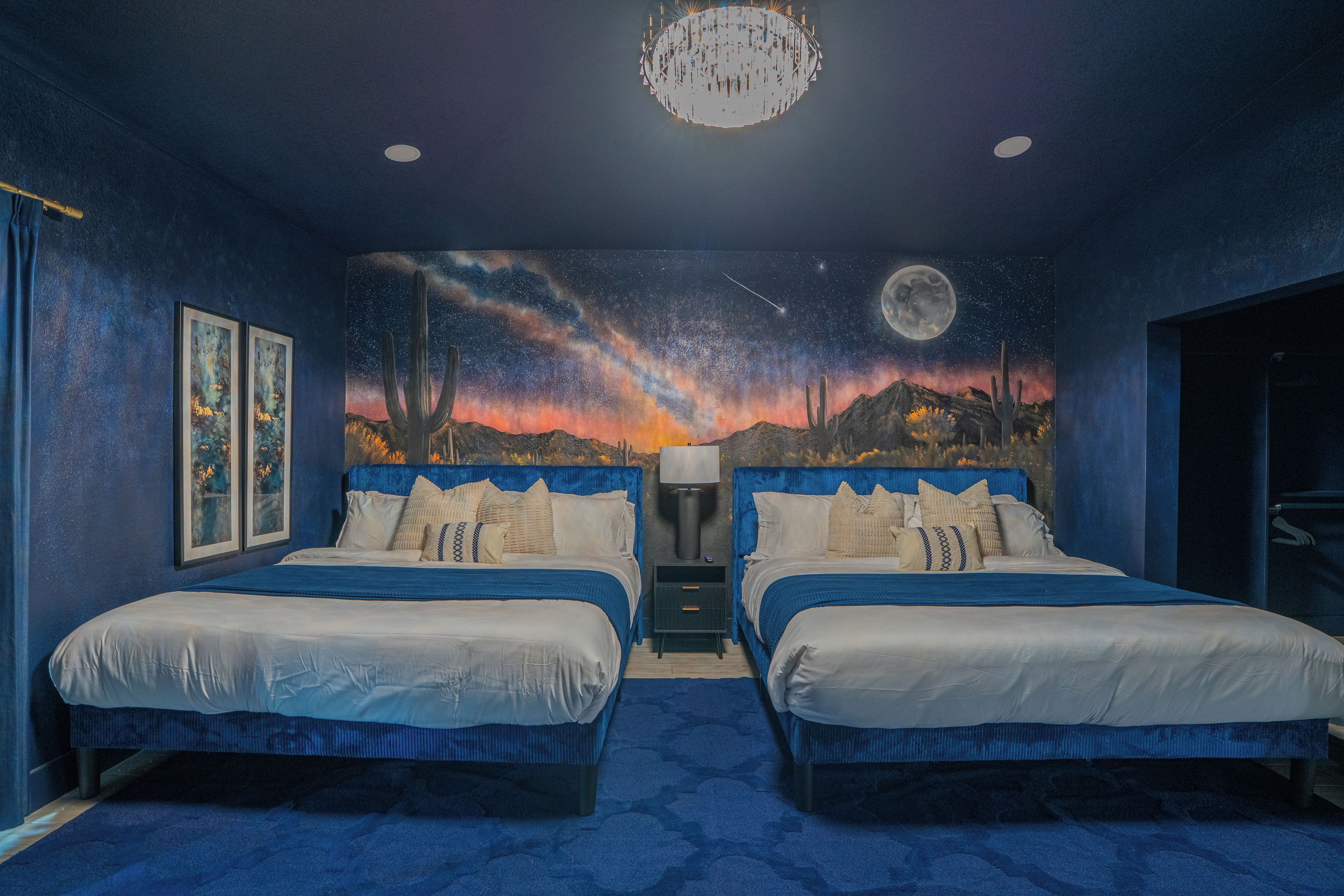 Een slaapkamer met twee bedden, een muurschildering van een sterrennacht en een kroonluchter.
