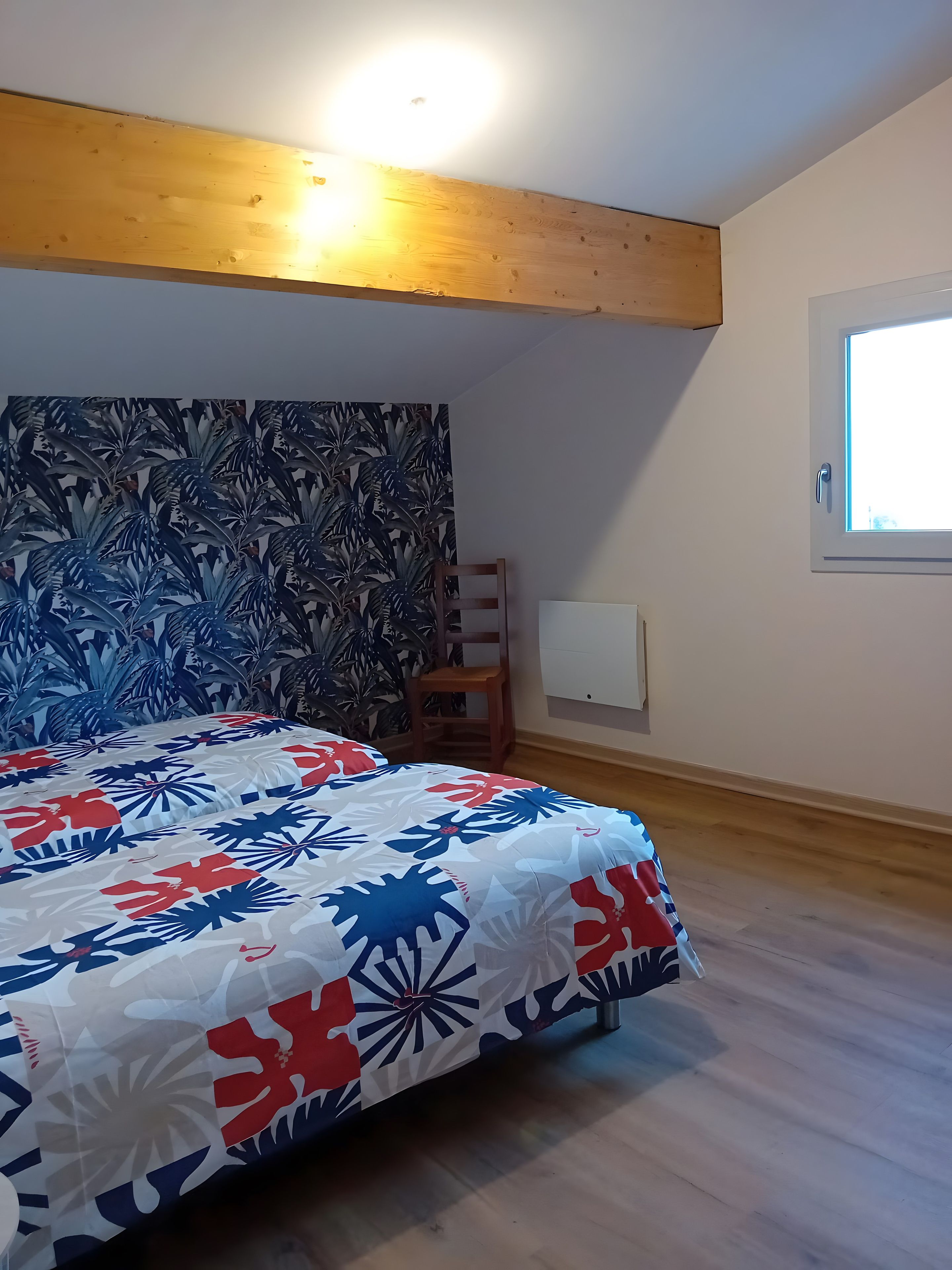 Une chambre à coucher avec un lit, un plafond en bois, une fenêtre et un mur orné d’un motif de feuilles.