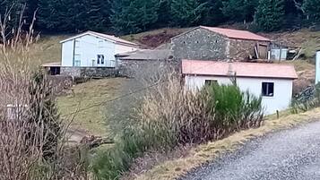 A rural setting with a gravel road, a white building with a red roof, and a stone structure in the background.