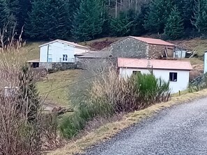 A rural setting with a gravel road, a white building with a red roof, and a stone structure in the background.