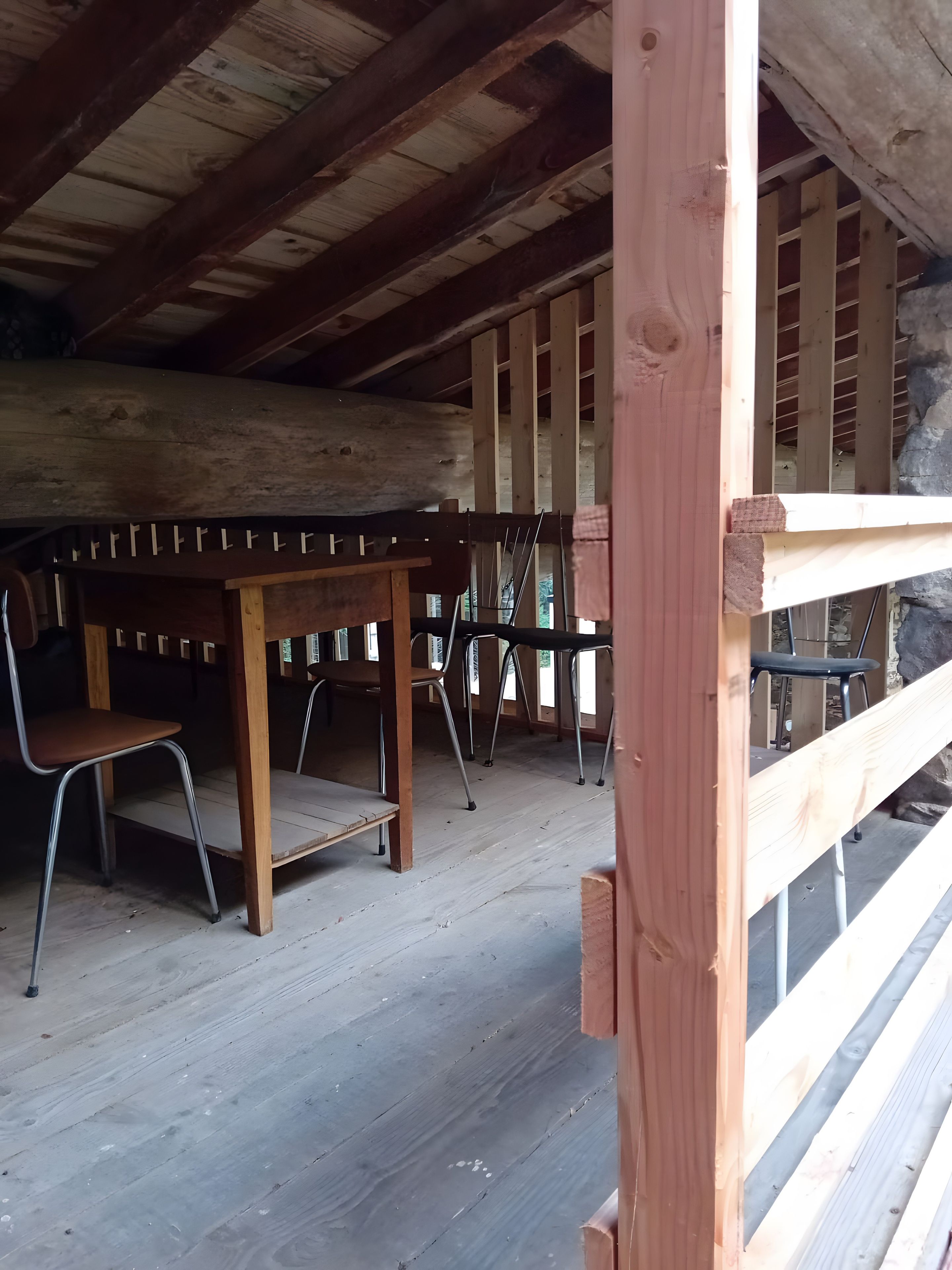A wooden interior with a high ceiling, a table with chairs, and a stone wall.