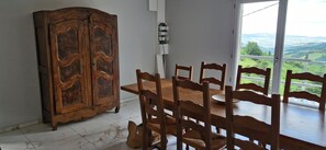 Ein Essbereich mit Holztisch und Stühlen, einem Schrank und Blick auf eine Landschaft durch ein Fenster.