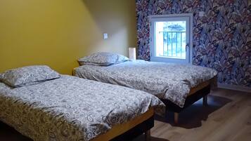 A room with two beds, wooden flooring, a window with a view, and a patterned wall.