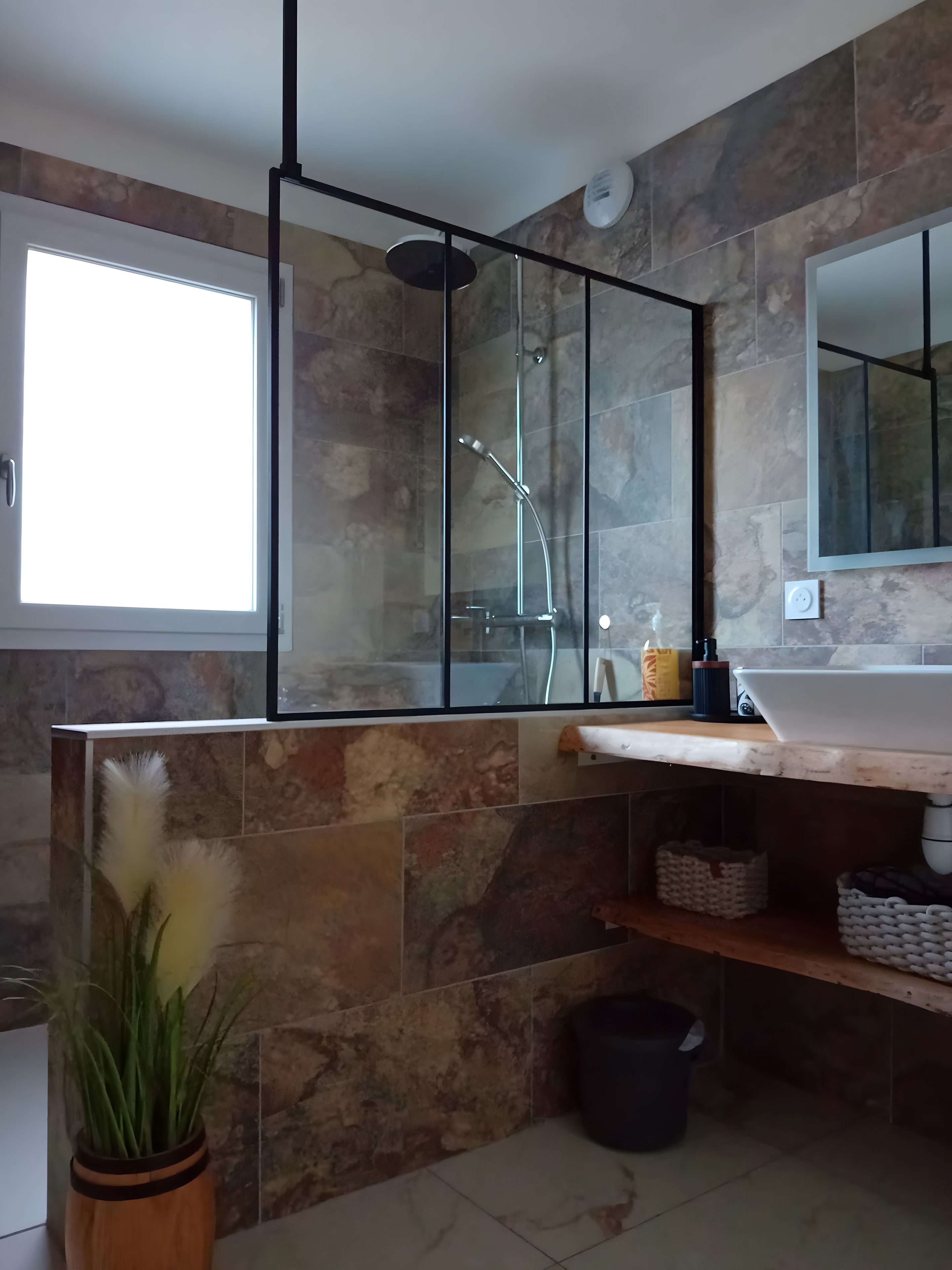 Un baño moderno con cabina de ducha de vidrio, un espejo grande y una pared con textura de piedra.