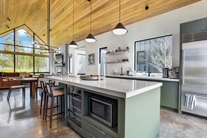 A modern kitchen with a central island, bar stools, and a large window providing a view of the outdoors.