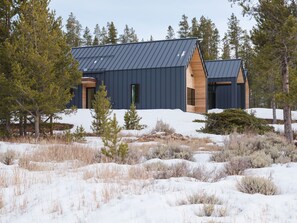 A modern building with a sloped roof, surrounded by snow and trees.