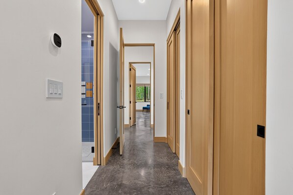 A hallway with wooden doors and a grey floor, leading to a room with a blue chair and a window.