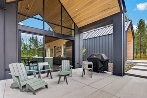 A modern outdoor patio with Adirondack chairs, a grill, and a view of the interior.