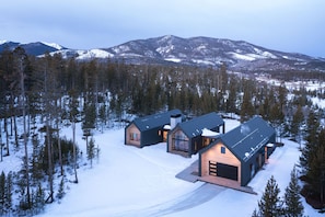 A modern cabin complex with multiple buildings, surrounded by a snowy forest and mountains in the background. - Two Sisters Secludes private home mt views in-floor heating family rental (Tabernash)