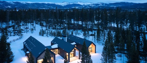 A modern cabin with multiple rooms, surrounded by a snowy forest and mountains in the background.
