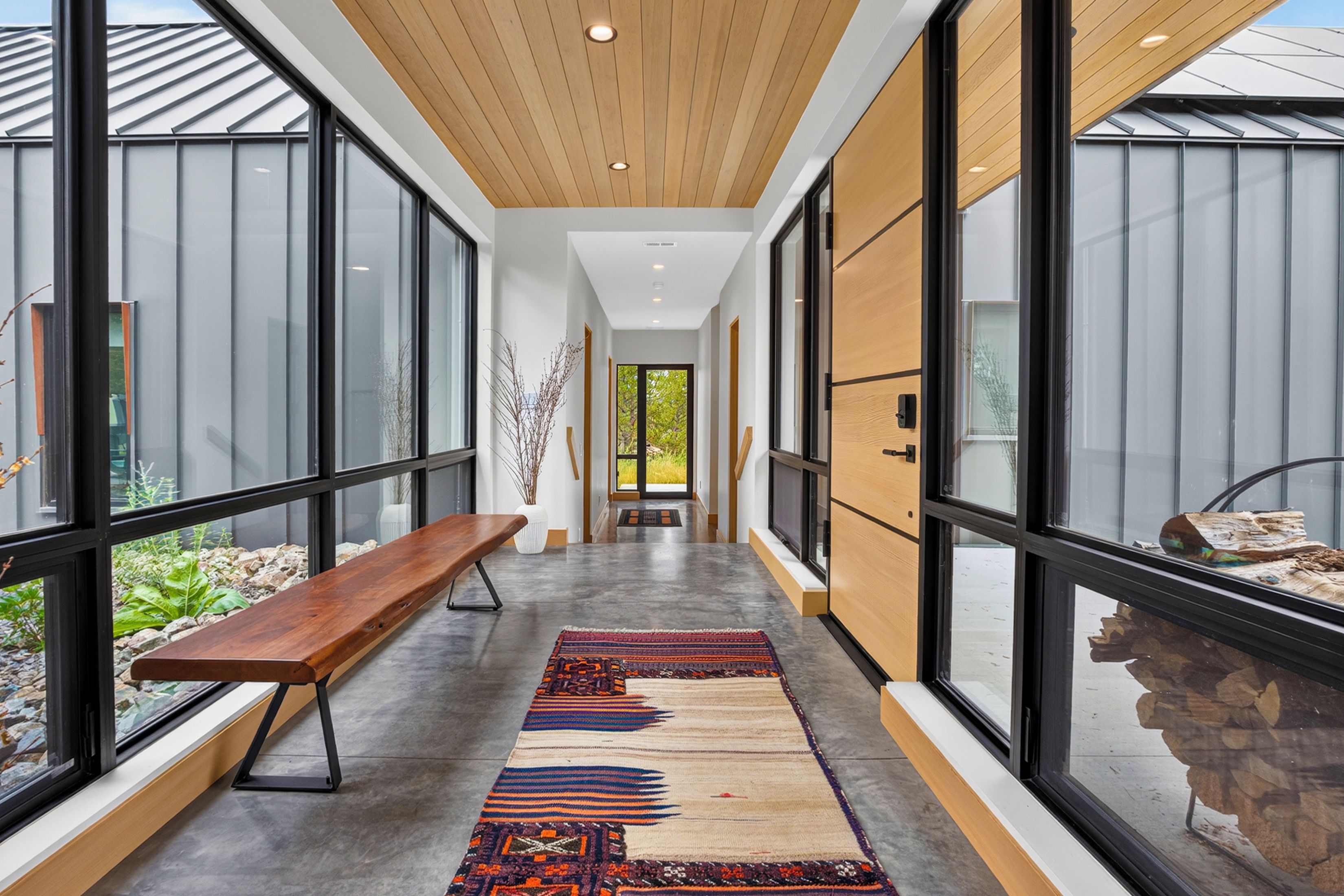 A modern interior with a long corridor, wooden benches, and large windows.