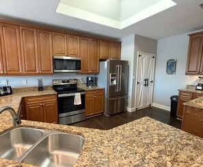 A kitchen with wooden cabinets, stainless steel appliances, granite countertops, and a double sink. - Mojito Haze- XL Townhome with Rooftop Sunsets, and Redington Beach Views! (Redington Shores)