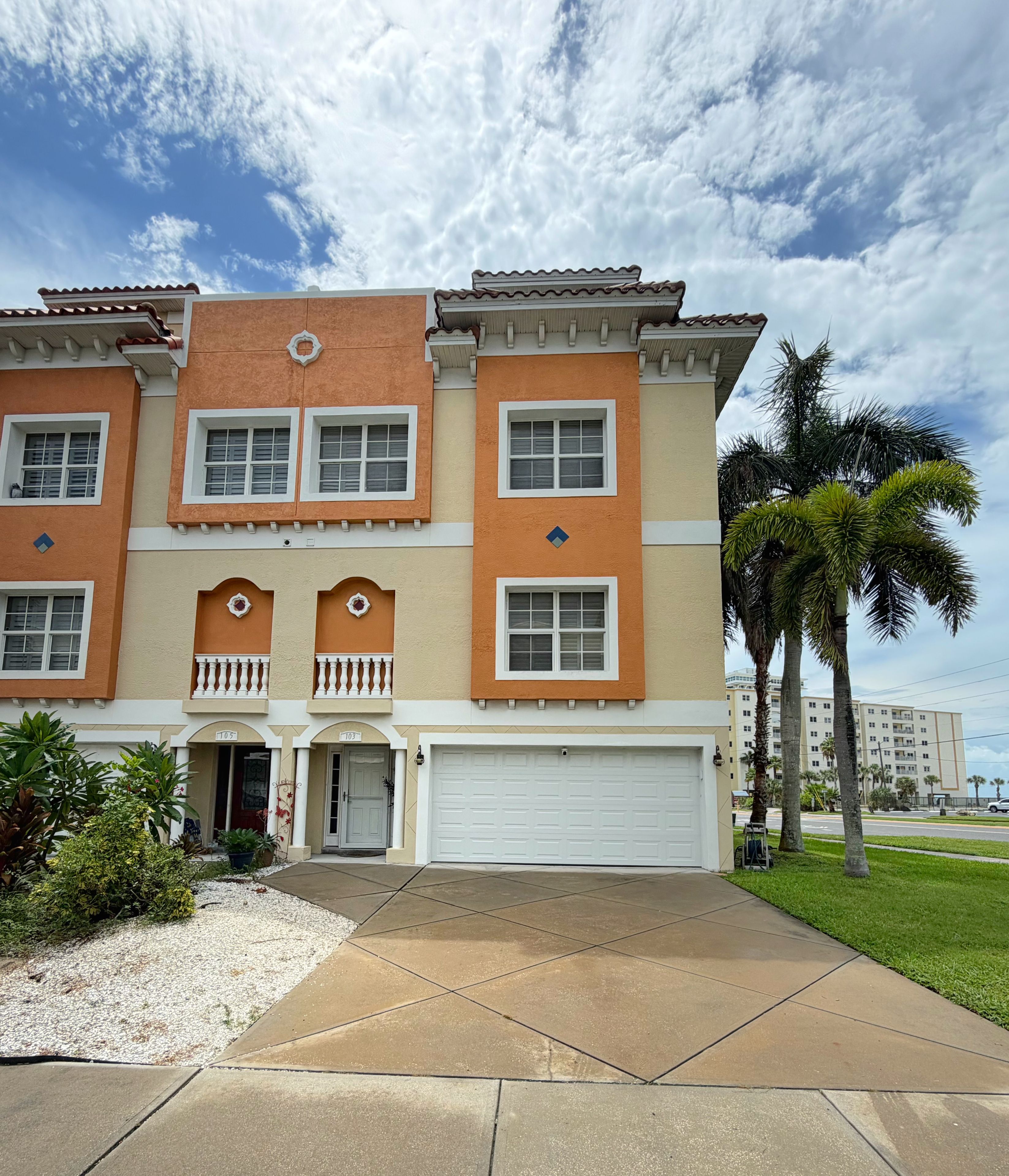 A multi-story residential building with a garage, a front porch, and a well-maintained lawn.