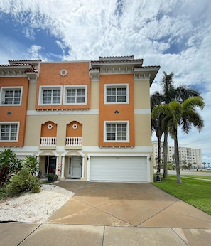 A multi-story residential building with a garage, a front porch, and a well-maintained lawn. - Mojito Haze- XL Townhome with Rooftop Sunsets, and Redington Beach Views! (Redington Shores)