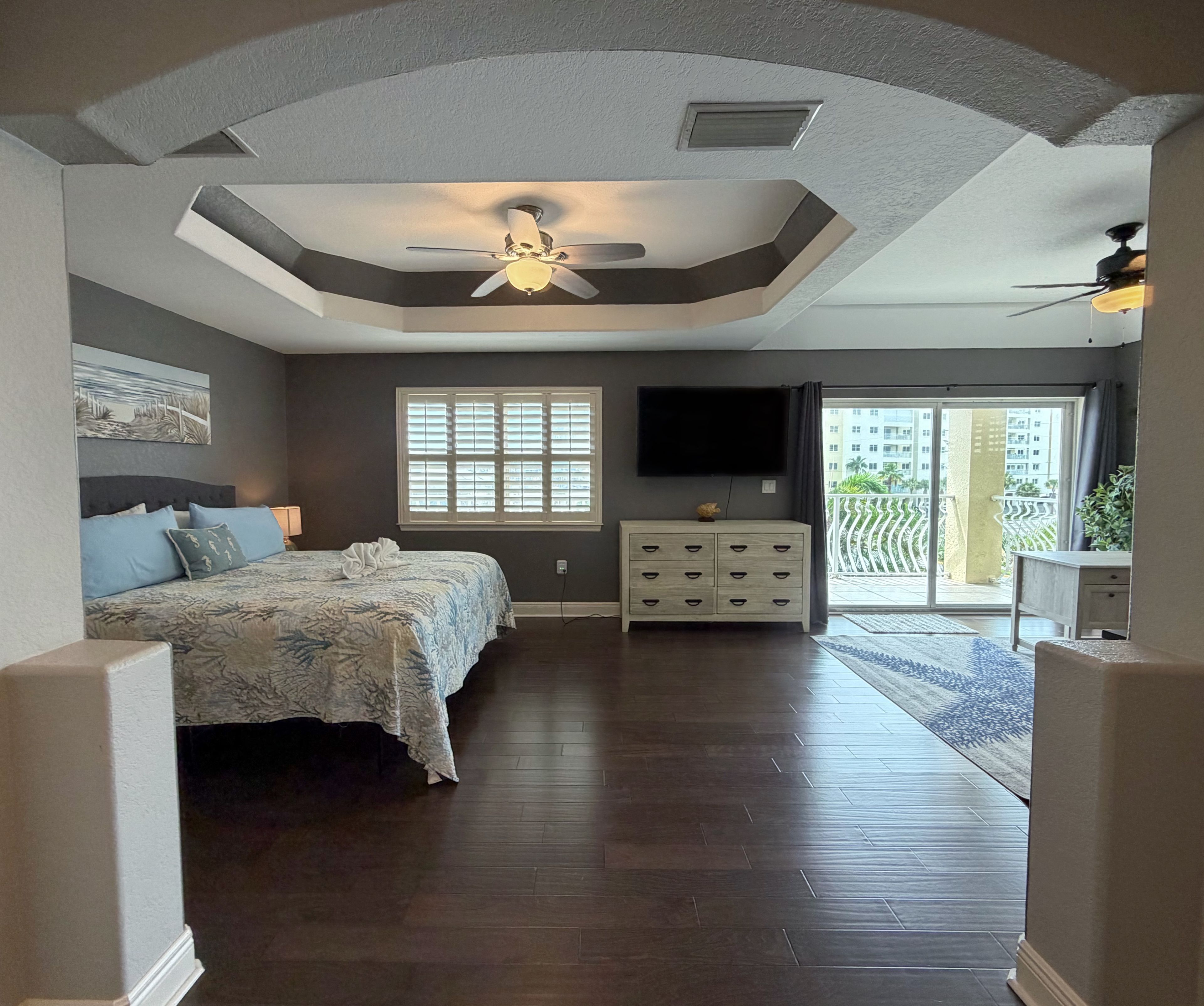 A bedroom with a bed, dresser, TV, and a ceiling fan.