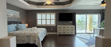 A bedroom with a bed, dresser, TV, and a ceiling fan.