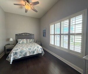 A bedroom with a bed, nightstand, lamp, ceiling fan, and a window with blinds. - Mojito Haze- XL Townhome with Rooftop Sunsets, and Redington Beach Views! (Redington Shores)