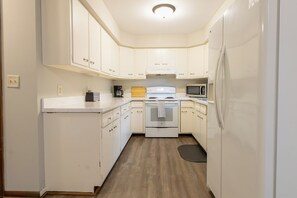 Una cucina compatta con mobili bianchi, forno, microonde e frigorifero.