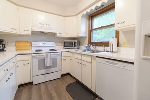 Una cocina con armarios blancos, estufa, microondas, pileta y ventana.