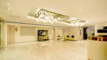 A spacious lobby with a marble floor, a reception desk, a sofa, and a decorative ceiling light fixture.