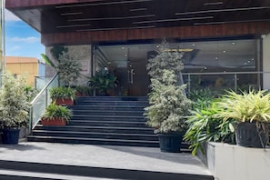 A building entrance with a staircase leading up to a glass door, surrounded by potted plants.