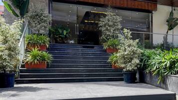 A building entrance with a set of stairs leading up to a glass door. There are potted plants on either side of the stairs.