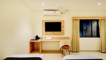 A hotel room with two beds, a desk with a chair, a television, and a window with curtains.