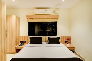 A hotel room with a large bed, two bedside tables, a wardrobe, a window with a view, and an air conditioning unit.