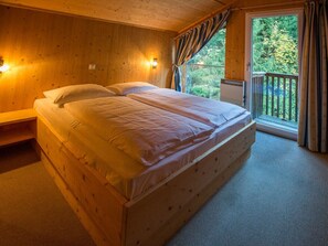 A wooden room with a bed, a nightstand, a window with curtains, and a view of trees. - Cabin in Annaberg With Swimming Pool (Annaberg-Lungoetz)