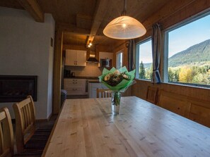 A wooden dining table with chairs, a vase with flowers, and a view of a forest through a window. - Cabin in Annaberg With Swimming Pool (Annaberg-Lungoetz)