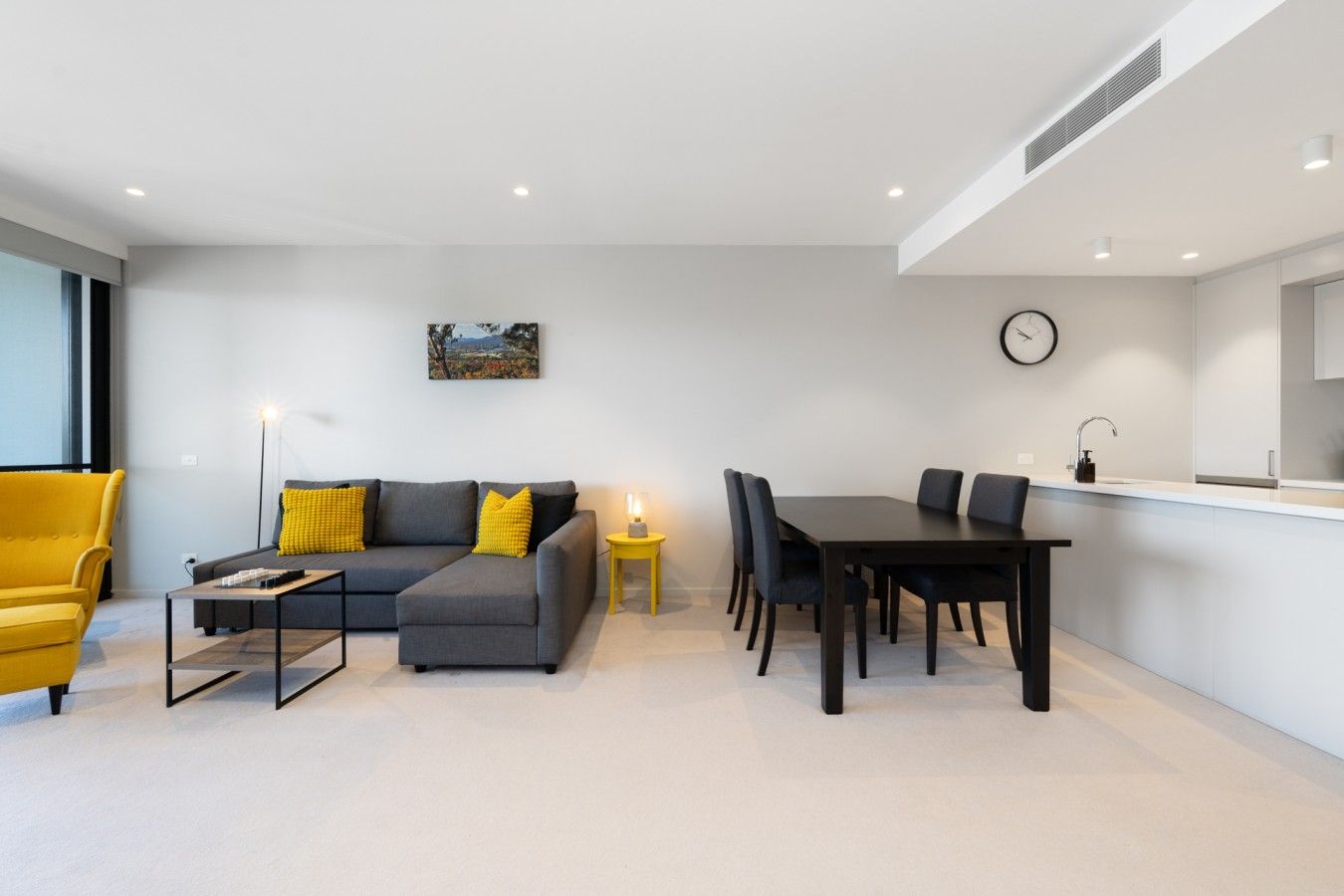Una sala de estar moderna con un sofá, una mesa de comedor y sillas. Hay un cuadro en la pared y un reloj.