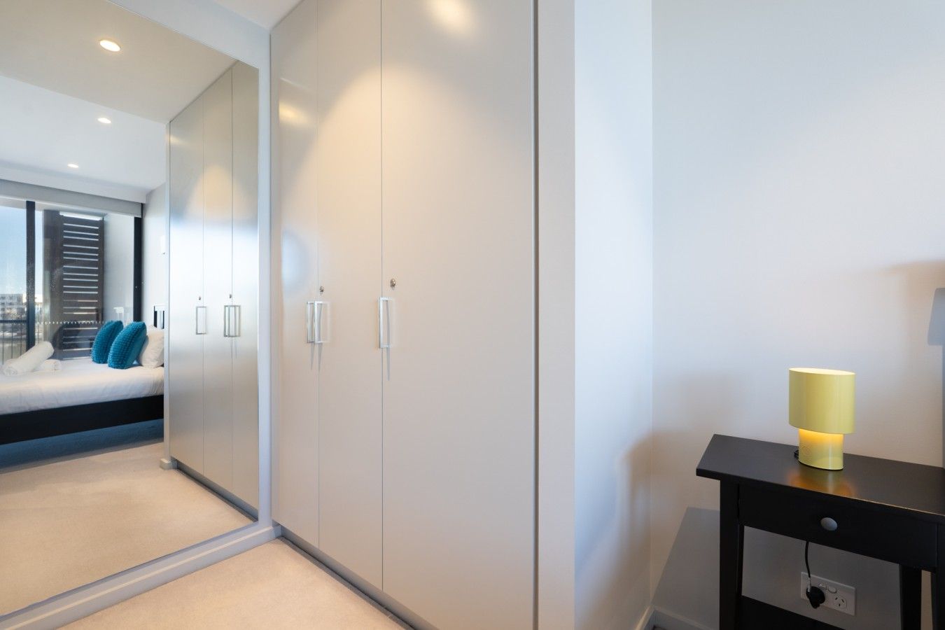 Un dormitorio moderno con cama, armario, mesita de noche y lámpara.