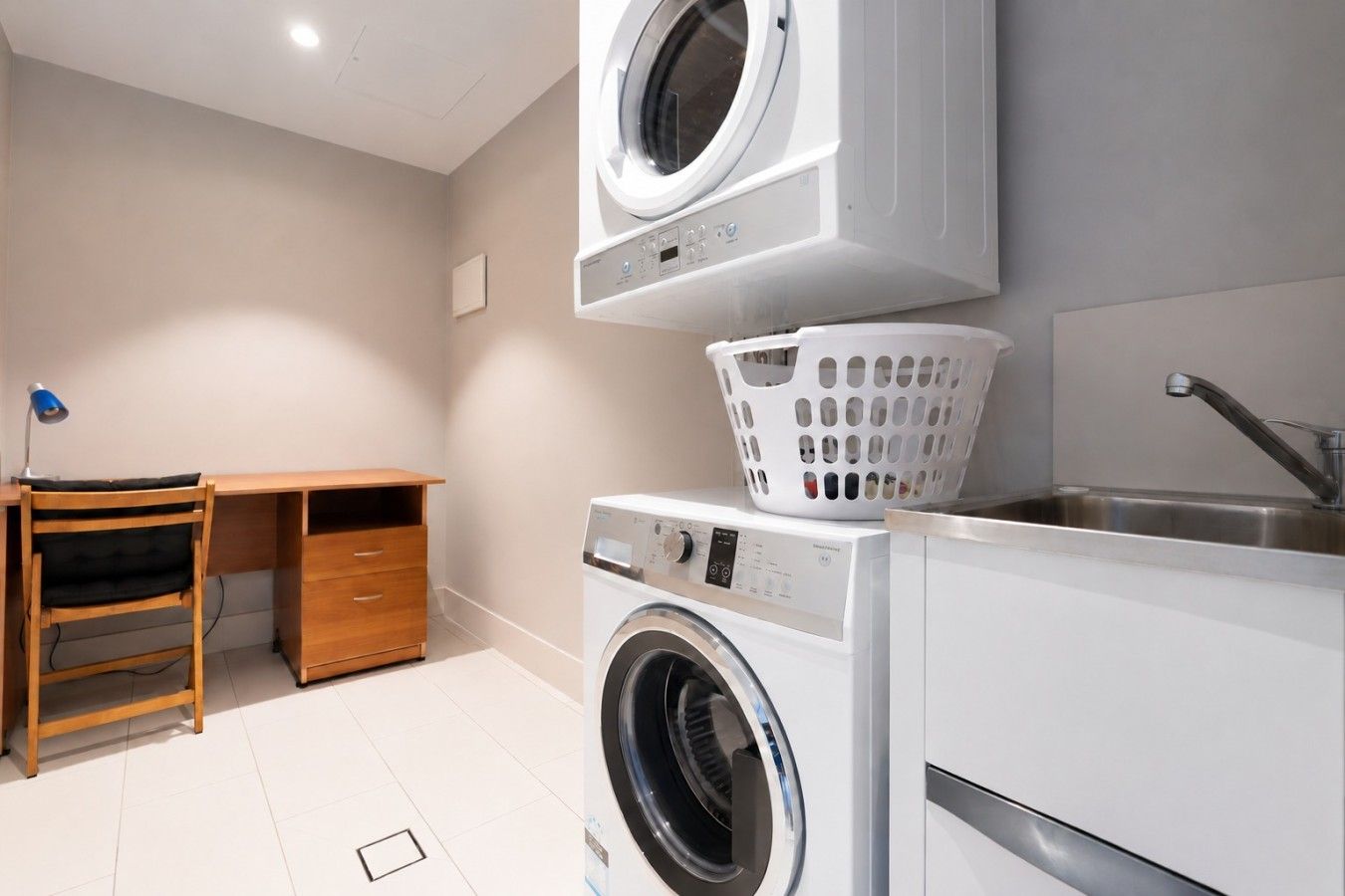 Un cuarto de lavandería con lavadora, secadora, lavabo y un escritorio de madera con silla.