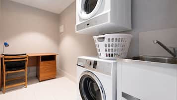 Un cuarto de lavandería con lavadora, secadora, lavabo y un escritorio de madera con silla.