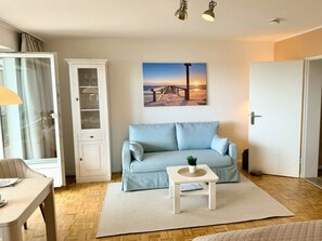 Sala de estar com sofá azul claro, armário branco, pintura de um pôr do sol e piso de madeira.