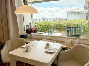 A hotel room with a dining table set for two, a window with a view of a pier and greenery, and a hanging lamp. - Holiday Apartment With 1 Bedroom (Wyk auf Foehr)