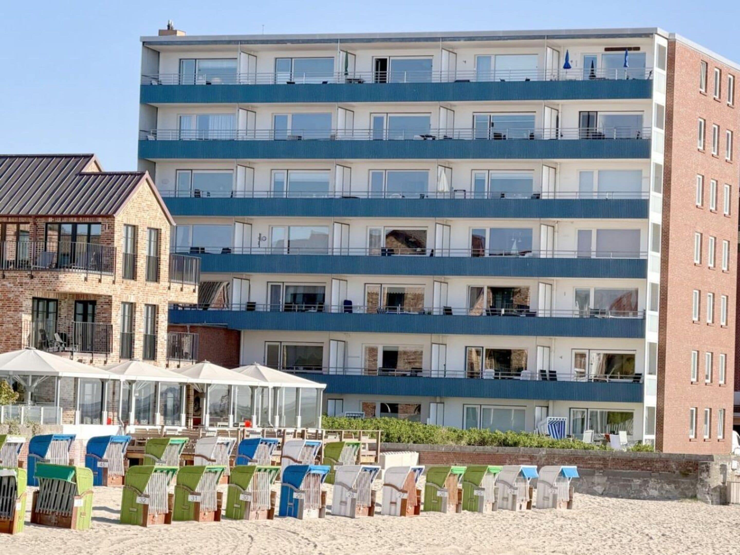 A multi-story hotel with balconies, a beachside location, and beach chairs.