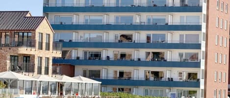 A multi-story hotel with balconies, a beachside location, and beach chairs.