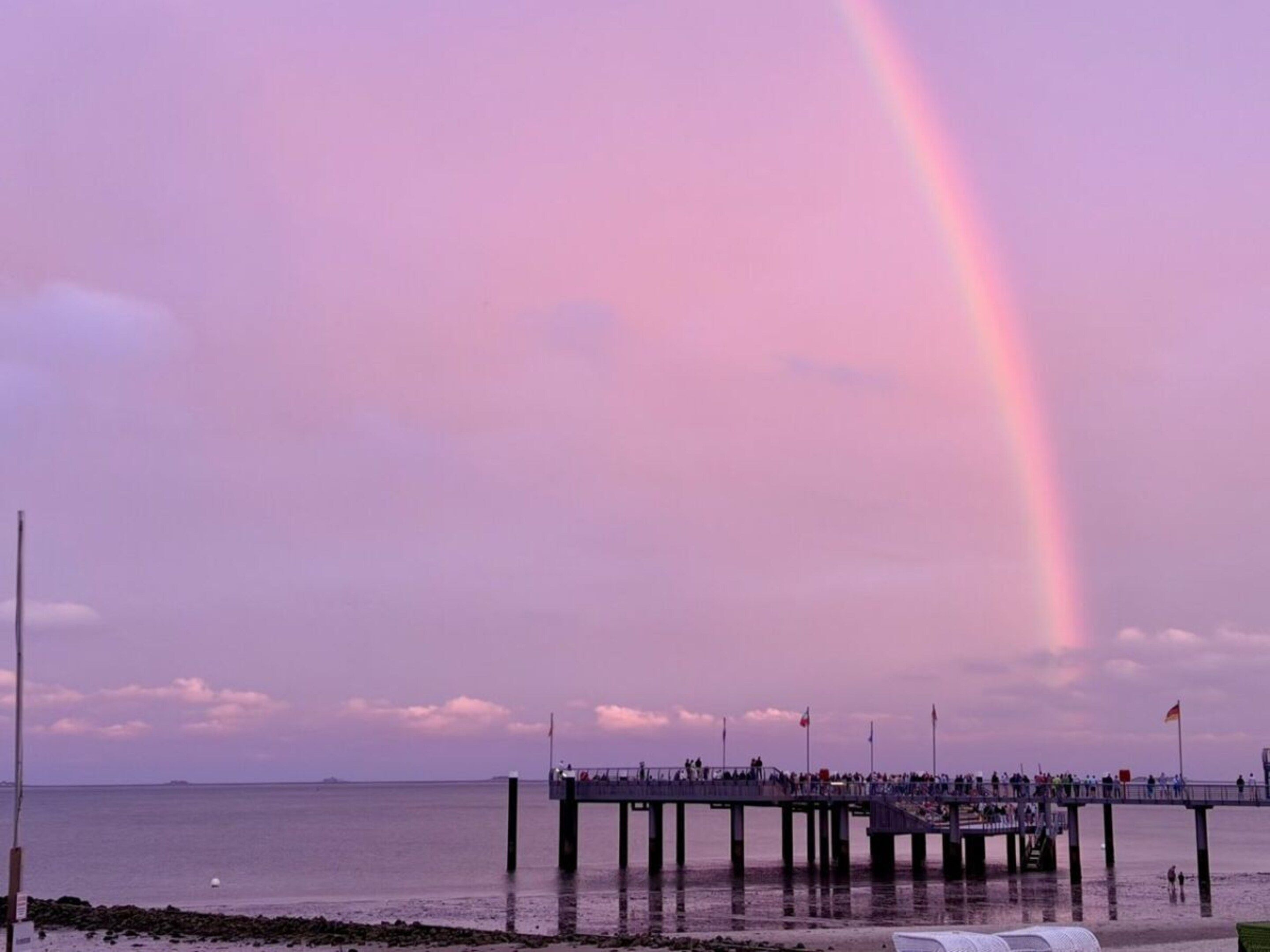 Un muelle se adentra en una masa de agua con un arcoíris en el cielo.